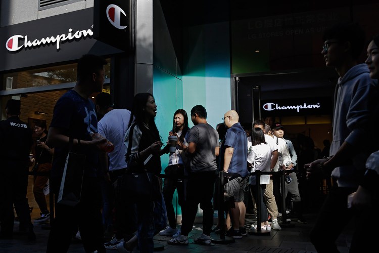 People walk by shoppers who wait in line to enter a store selling sportswear by American brand Champion, at the capital city's popular shopping mall in Beijing on Monday. China raised tariffs Monday on thousands of U.S. goods in an escalation of its fight with President Trump over technology policy, and it accused Washington of bullying Beijing and damaging the global economy. 