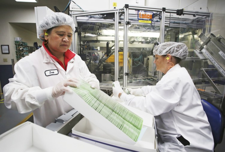 production specialist Sea Neak, left, works with trainee Patricia Phillips as they batch product in boxes for quality-control testing last week. Staff photo by Jill Brady