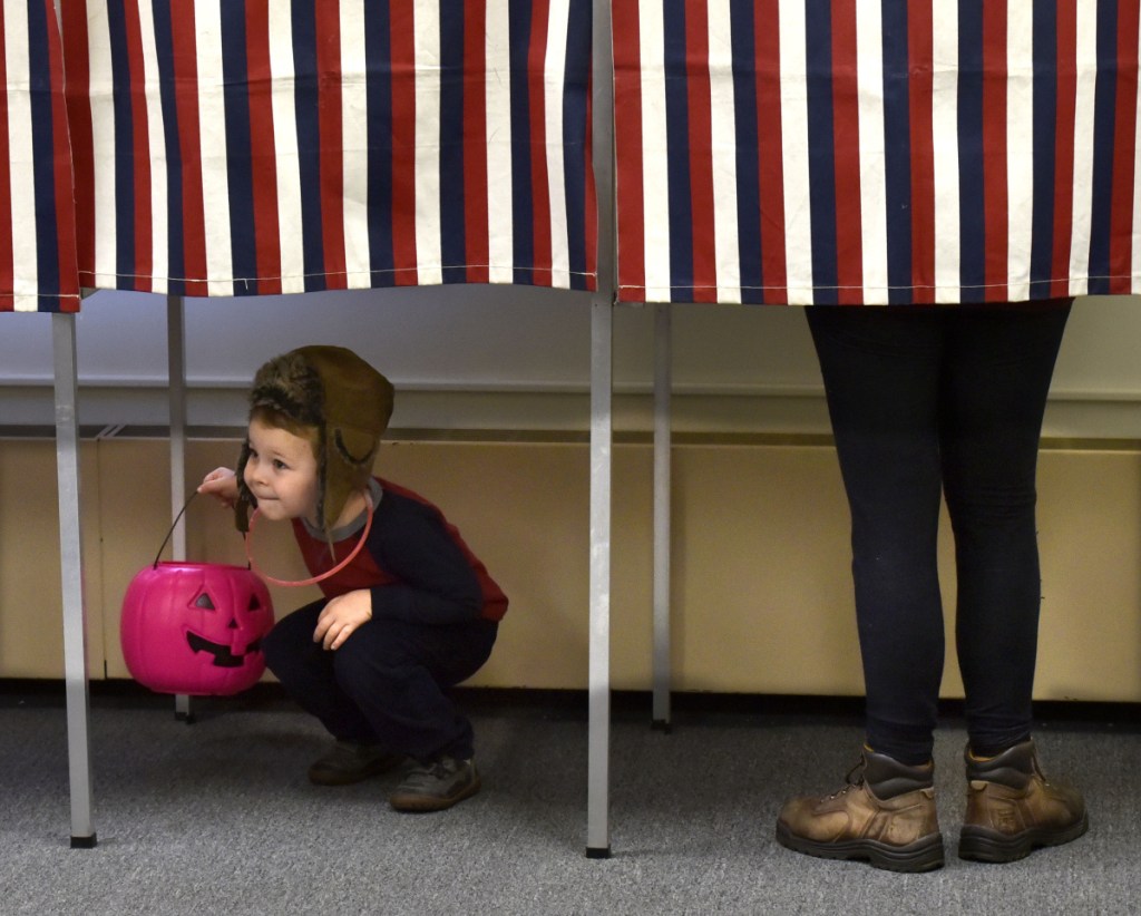 As Dorene Neal fills out her ballot Tuesday, her son Gilroy looks under the drape at other voters at the Skowhegan Municipal building. Dorene said he always has his Halloween bucket with him.