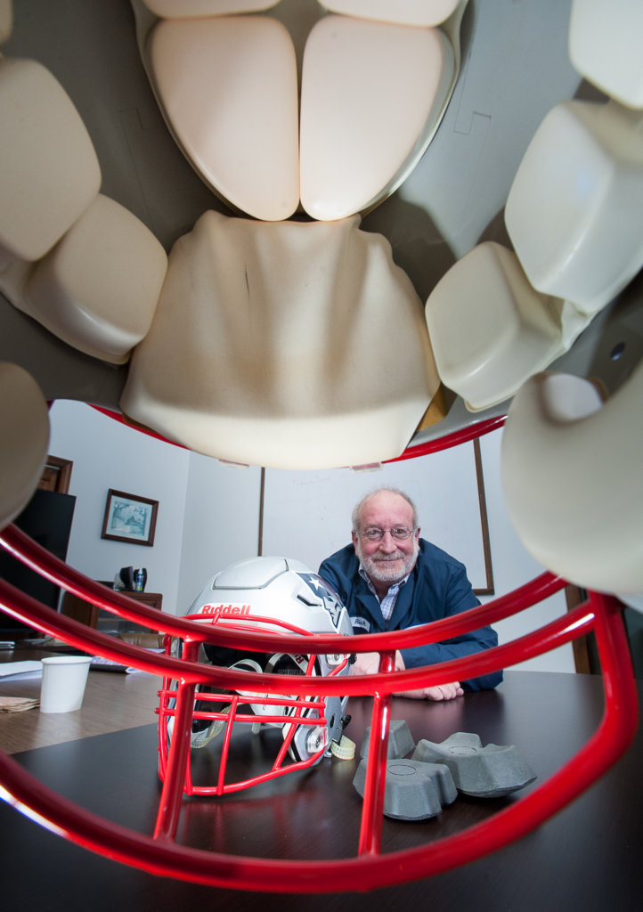 Rick House, technical director at Jones & Vining, is framed through an older-style football helmet Thursday at the company's facility in Lewiston. A helmet featuring the company's new, higher-protection padding rests in front of House.