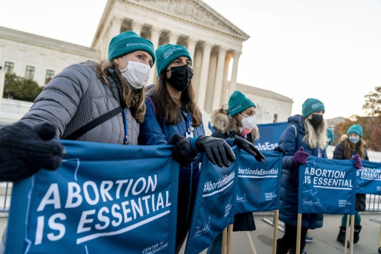 Abortion rights advocates hold signs that read "Abortion is Essential" as they demonstrate in front of the U.S. Supreme Court, Wednesday, Dec. 1, 2021, in Washington, as the court hears arguments in a case from Mississippi, where a 2018 law would ban abortions after 15 weeks of pregnancy, well before viability. 